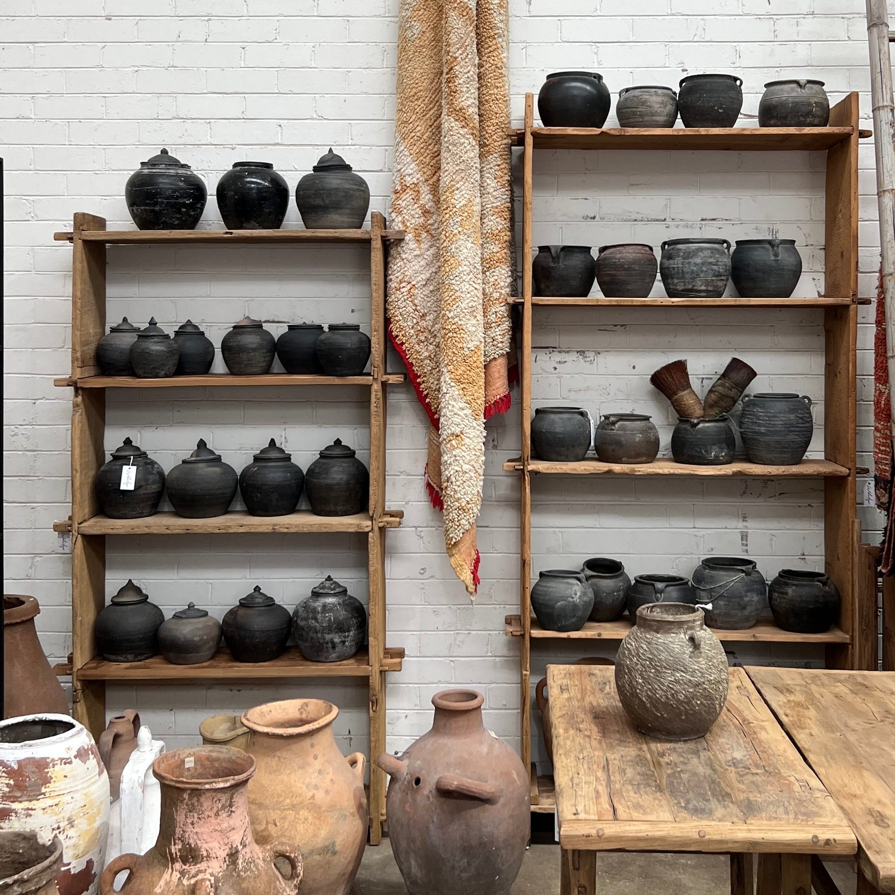 Wooden shelves with various ceramic pots against a white brick wall.
