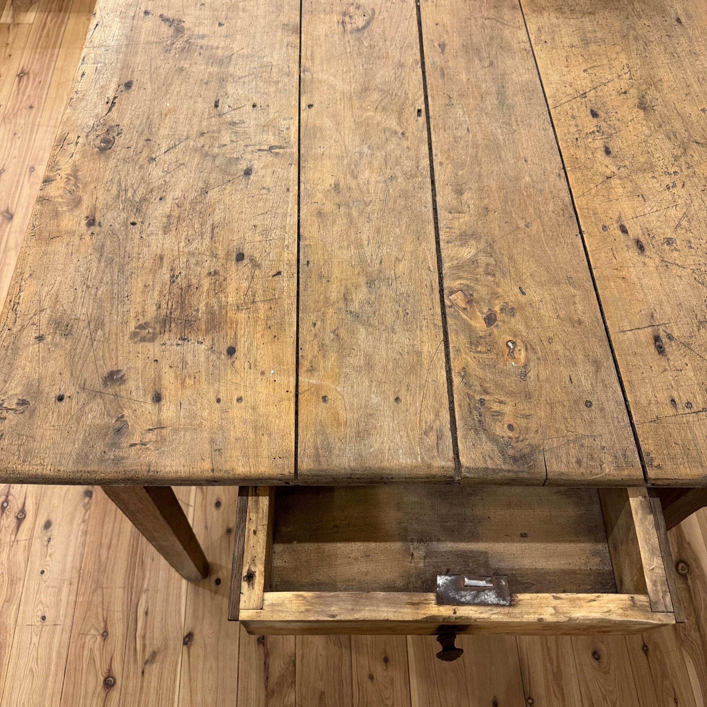 A rustic wooden table with a pull-out drawer, made from weathered natural wood planks, shown from a high angle on a wooden floor.